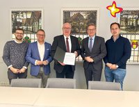 Fünf Männer stehen nebeneinder in der Reihe, der Mann in der Mitte zeigt eine Urkunde vor.