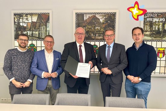 Fünf Männer stehen nebeneinande hinter einem Tisch. Der Mann in der Mitte hält eine Urkunde in den Händen.