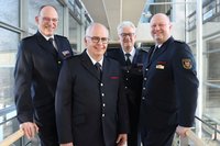 Vier Männer in Feuerwehruniform stehen nebeneinander und lächeln in die Kamera.