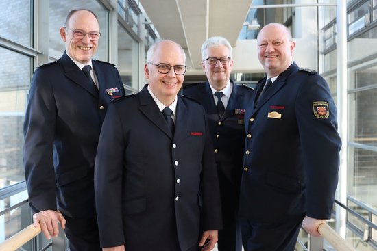 Vier Männer in Feuerwehruniform stehen nebeneinander und lächeln in die Kamera.