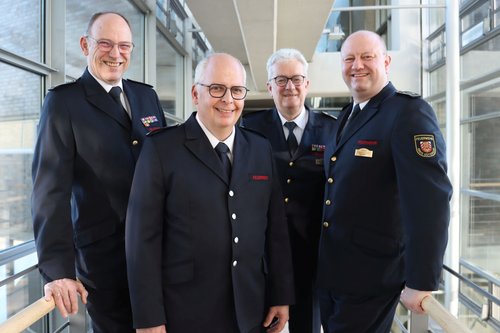 Vier Männer in Feuerwehruniform stehen nebeneinander und lächeln in die Kamera.