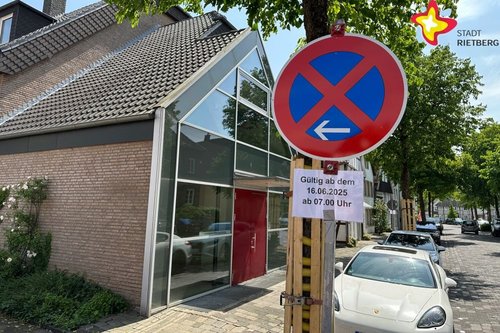 Zu sehen ist ein Parkverbotsschild mit dem Hinweis "Gültig ab dem 16.06.2025 ab 7 Uhr". Im Hintergrund stehen zwei geparkte Autos. Links im Bild ist das Pfarrheim zu sehen.
