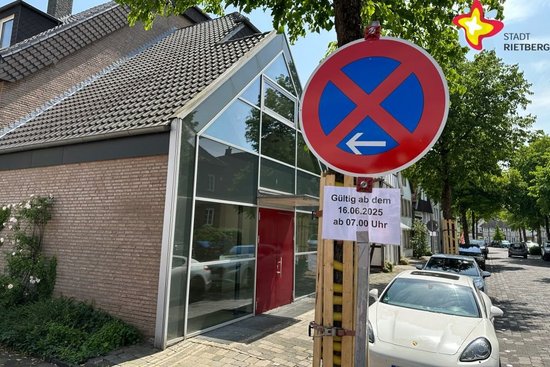 Zu sehen ist ein Parkverbotsschild mit dem Hinweis "Gültig ab dem 16.06.2025 ab 7 Uhr". Im Hintergrund stehen zwei geparkte Autos. Links im Bild ist das Pfarrheim zu sehen.