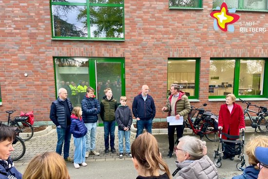 Bürgermeister Andreas Sunder steht mit einer Gruppe von Bürgerinnen und Bürgern vor einem Gebäude und erklärt etwas. Das Gebäude hat eine rote Klinkerfassade und grüne Fensterrahmen.