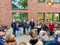 Bürgermeister Andreas Sunder steht mit einer Gruppe von Bürgerinnen und Bürgern vor einem Gebäude und erklärt etwas. Das Gebäude hat eine rote Klinkerfassade und grüne Fensterrahmen.