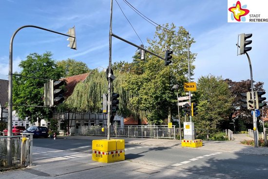 Das Foto zeigt die Rathausstraße und eine Ampel. Die Sonne scheint, oben rechts im Bild sind parkende Autos sowie Gebäude zu sehen.