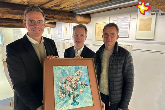 Die drei genannten Männer stehen auf der Galerie des Kundthauses und halten ein Bild in die Kamera. Es zeigt gemalte Blumen. Alle Männder lächeln.