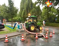 Ein grüner Traktor steht am Straßenrand. Rot-weiß gestreifte Pilonen stehen um einen geöffneten Gullideckel herum.