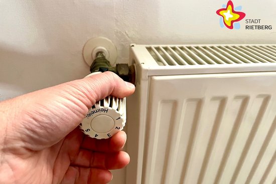 Eine Hand dreht den Knopf an einer Heizung.