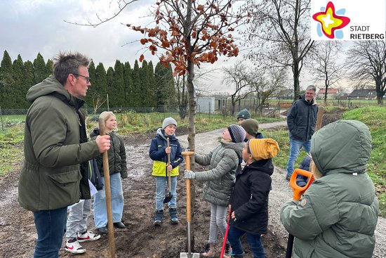 Kinder und Bürgermeister Andreas Sunder haben Schaufeln in der Hand und stehen um ihren Baum herum, der gerade eingepflanzt worden ist.