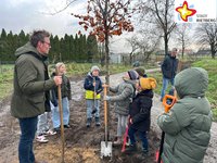 Kinder und Bürgermeister Andreas Sunder haben Schaufeln in der Hand und stehen um ihren Baum herum, der gerade eingepflanzt worden ist.