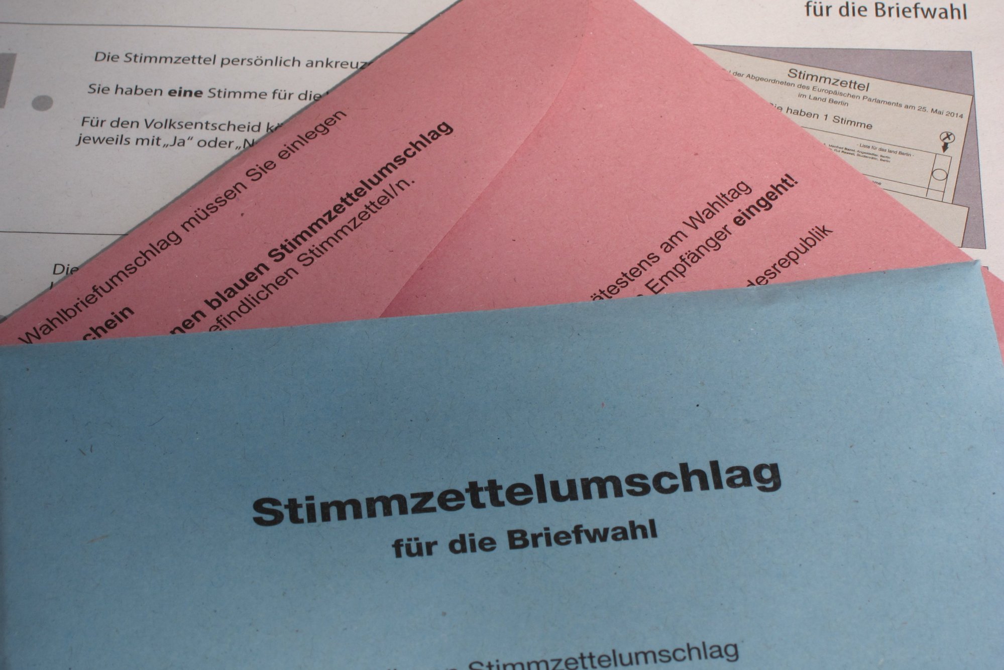 Ein roter Briefumschlag lugt unter einem blauen Umschlag mit der Aufschrift Briefwahl hervor.