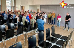 Dutzende Frauen und Männer stehen zwischen Stuhl- und Tischreihen in der Aula und lauschen den Erläuterungen von Ingmar Schmidt, der etwas abseits steht.