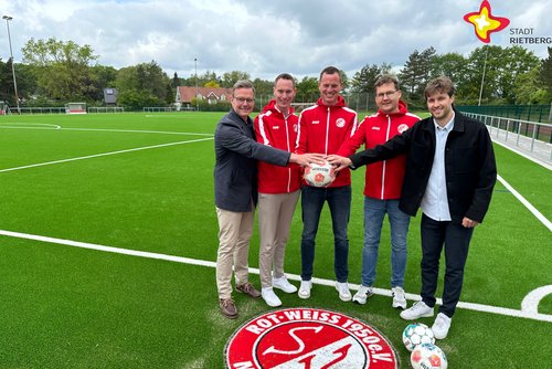 Die genannten Personen halten einen Fußball in der Hand und schauen in die Kamera. Im Hintergrund ist der Fußballplatz zu sehen, im Vordergrund das Logo von Rot-Weiß Mastholte.