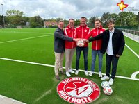 Die genannten Personen halten einen Fußball in der Hand und schauen in die Kamera. Im Hintergrund ist der Fußballplatz zu sehen, im Vordergrund das Logo von Rot-Weiß Mastholte.