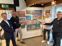 Die genannten Personen zeigen auf bunte Bilder von James Rizzi, die an einer Wand im Museum hängen. Sie schauen in die Kamera.