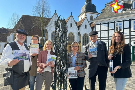 Gästeführer und Touristik-Mitarbeiterinnen stehen am Stadtbrunnen mit Vögeln. Im Hintergrund sind Teile des Historischen Rathauses und die Pfarrkirche zu sehen.