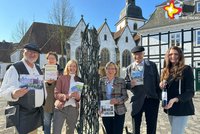Gästeführer und Touristik-Mitarbeiterinnen stehen am Stadtbrunnen mit Vögeln. Im Hintergrund sind Teile des Historischen Rathauses und die Pfarrkirche zu sehen.