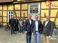Neun Frauen und Männer stehen nebeneinander vor einer gelben Fachwerkfassade.