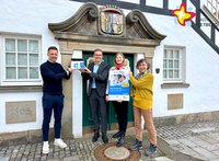Mario Aschhoff und Bürgermeister Andreas Sunder halten symbolisch eine Blaue Hausnummer an das Historische Rietberger Rathaus. Rietbergs Klimaschutzmanagerin Wibke Kordtomeikel und Michaela Prelle von der Energieberatung der Verbraucherzentrale NRW stehen daneben und halten ein Werbeplakat in den Händen.