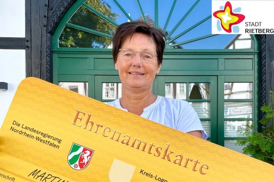 Doris Vogel, eine Mitarbeiterin der Bürgerstiftung Rietberg, hält eine überdimensionale, goldfarbene Ehrenamtskarte in die Kamera.