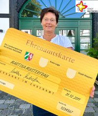 Doris Vogel, eine Mitarbeiterin der Bürgerstiftung Rietberg, hält eine überdimensionale, goldfarbene Ehrenamtskarte in die Kamera.