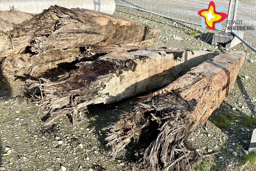 Mehrere massive und alte Holzpflöcke liegen gestapelt über- und nebeneinander.