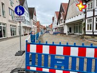 Eine Warnbake steht vor einer im Bau befindlichen Straße. Links der Fußweg ist bereits ordentlich gepflastert.