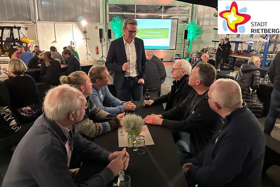 Mehrere Männer sitzen in einer Halle des Rietberger Bauhofs auf Bänken und sprechen mit Bürgermeister Andreas Sunder.