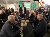 Mehrere Männer sitzen in einer Halle des Rietberger Bauhofs auf Bänken und sprechen mit Bürgermeister Andreas Sunder.