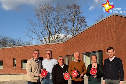 Die genannten Personen stehen vor dem Neubau und schauen in die Kamera. Der Neubau ist rot geklinkert, die Sonne schein.