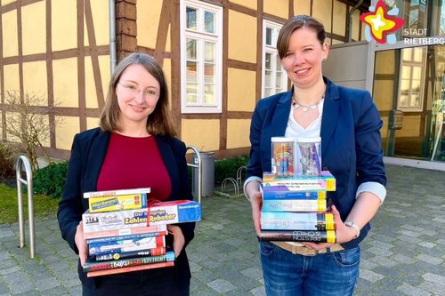 Die Leiterinnen der Stadtbibliothek Rietberg mit Büchern und anderen Medien in der Hand vor dem Gebäude, in dem die Einrichtung beheimatet ist.