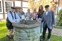 Gästeführer und Mitarbeiterinnen der Touristikinformationen stehen am Brunnen im Garten des Heimathauses.