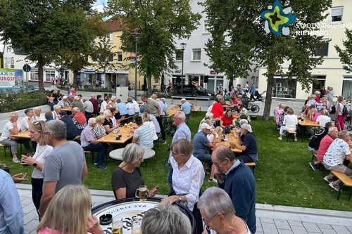 Menschen sitzen gut gelaunt an Biertischen auf einer grünen Wiese.