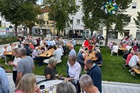 Menschen sitzen gut gelaunt an Biertischen auf einer grünen Wiese.