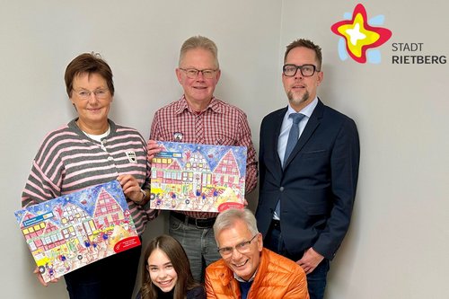 Ein Mädchen, drei Männer und eine Frau stehen und knien hinter einem mit grünem Stoff ausgeschlagenen Kasten voller weißer Plättchen.