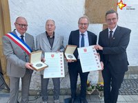 Ribéracs Bürgermeister Nicolas Platon, die beiden Verdienstmedaillenträger Jean Helmer und Bernhard Altehülshorst sowie Bürgermeister Andreas Sunder halten stehend Medaillen und Urkunden in den Händen und schauen in die Kamera.