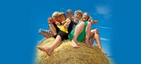 Fünf Mädchen und Jungen sitzen lachend vor blauem Himmel auf einem Strohballen.