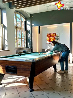 Ein Mann lehnt mit einem Queue in den Händen über einem Billardtisch.