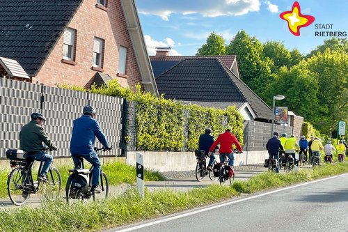 Mehrere Menschen sind auf Fahrrädern auf einem Radweg in einer Wohnsiedlung unterwegs, von hinten fotografiert.