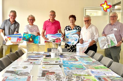 Heinrich Rasche, Anja Rodenbeck, Norbert Laumeier, Doris Vogel, Bertwald Adrian und Otto Hartmann stehen nebeneinander mit von Kindern gemalten Bildern in den Händen. Auf dem Tisch vor ihnen liegen ordentlich nebeneinander zahlreiche weitere solcher Kinderbilder.