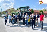 Mehrere Akteure haben sich vor einem Traktor auf dem Parkplatz neben dem Schnäppchen-Markt in Rietberg positioniert, um mit Blumen in der Hand auf die anstehende Wirtschaftsschau hinzuweisen.