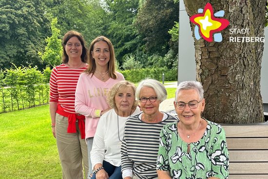 Fünf Frauen stehen und sitzen hintereinander in einer Reihe und blicken in die Kamera.