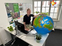 Wibke Kordtomeikel steht an ihrem Schreibtisch und hält einen großen Erdball in der Hand. Sie schaut in die Kamera.
