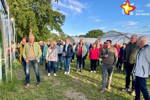 Mehrere Menschen stehen im Halbkreis und lauschen einem Sprecher mit einem Mikrofon in der Hand.