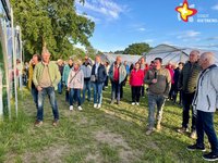 Mehrere Menschen stehen im Halbkreis und lauschen einem Sprecher mit einem Mikrofon in der Hand.