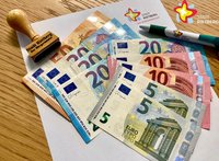 Mehrere Euro-Scheine liegen aufgefächert auf einem weißen Blatt Papier, daneben ein Stempel und ein Kugelschreiber mit der Aufschrift "Stadt Rietberg"