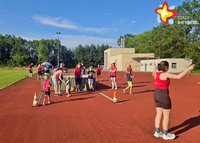 Viele Menschen unterschiedlichen Alters stehen auf einer roten Tartanbahn eines Sportplatzes. Zwei von ihnen versuchen sich im Seilspringen.