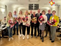 Fünf Frauen und fünf Männer stehen lächelnd nebeneinender und halten Blumen in den Händen.