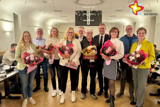 Fünf Frauen und fünf Männer stehen lächelnd nebeneinender und halten Blumen in den Händen.